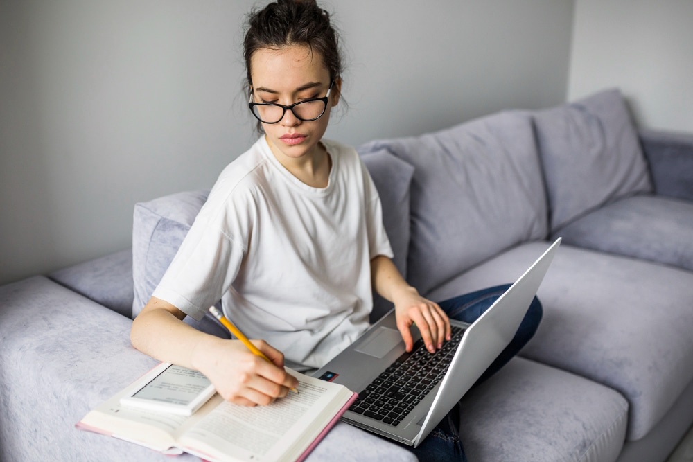 woman with laptop making notes in book